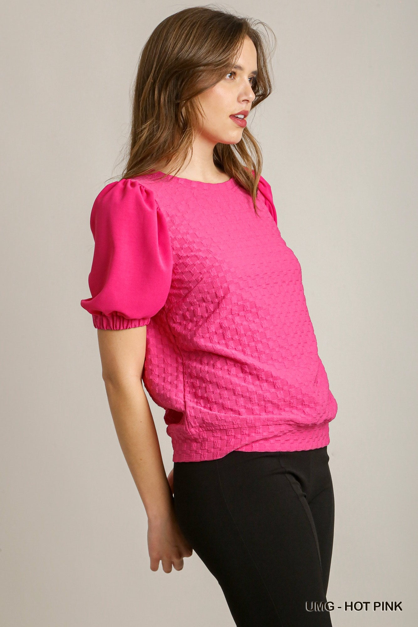 Woman wearing a bright pink textured top with puffed sleeves on a plain background