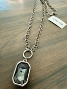 Necklace with a pendant on a wooden surface, featuring a visible brand tag.