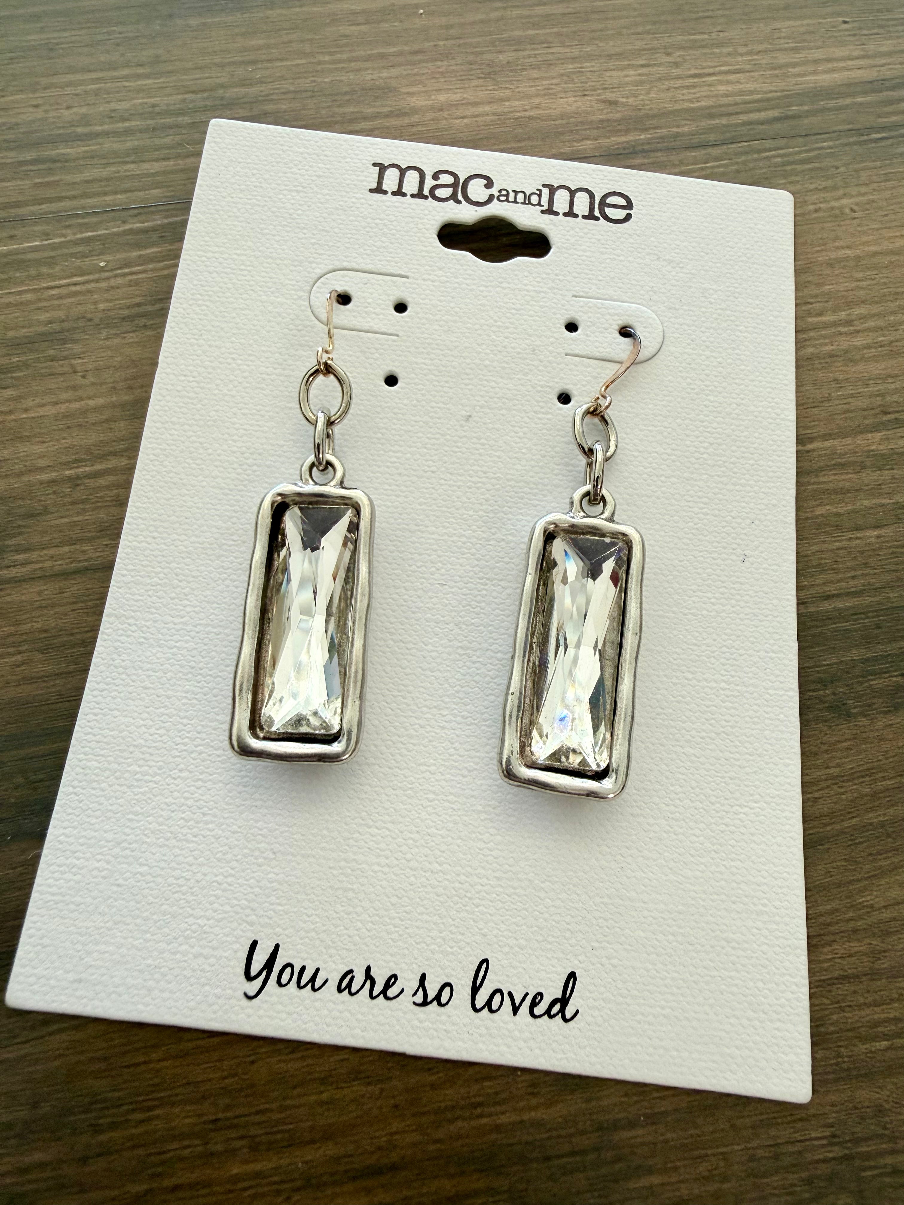 Silver earrings on a 'mac and me' branded card with text on a wooden surface