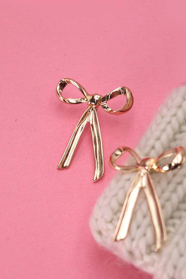 Gold bow-shaped earrings on a pink background