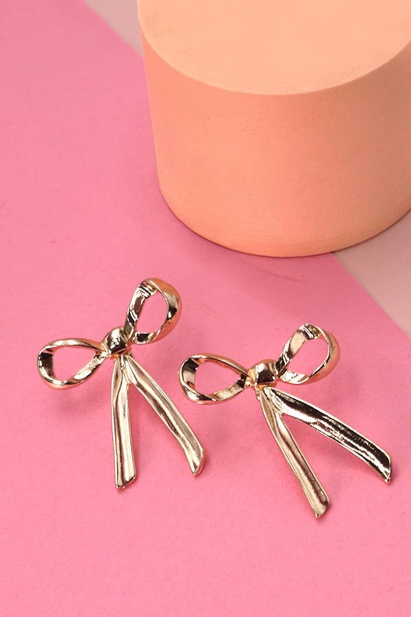Gold bow-shaped earrings on a pink background