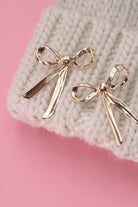 Gold bow-shaped earrings on a textured surface with pink background
