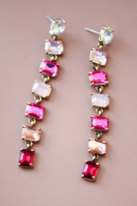 Pair of long earrings with pink and red gemstones on a beige background