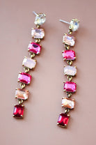 Pair of long earrings with pink and red gemstones on a beige background