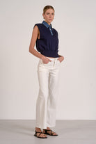 Woman wearing a navy sleeveless top and white pants against a plain background