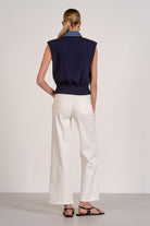 Person wearing a navy sleeveless top and white pants on a plain background