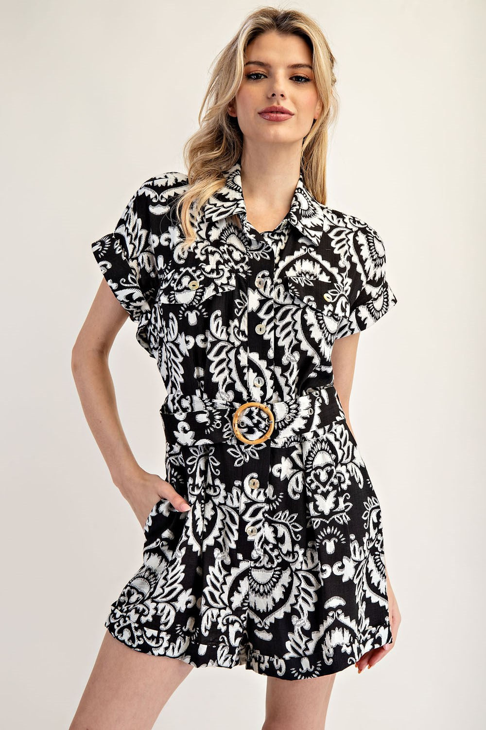 Woman wearing a black and white patterned dress with a belt on a plain background