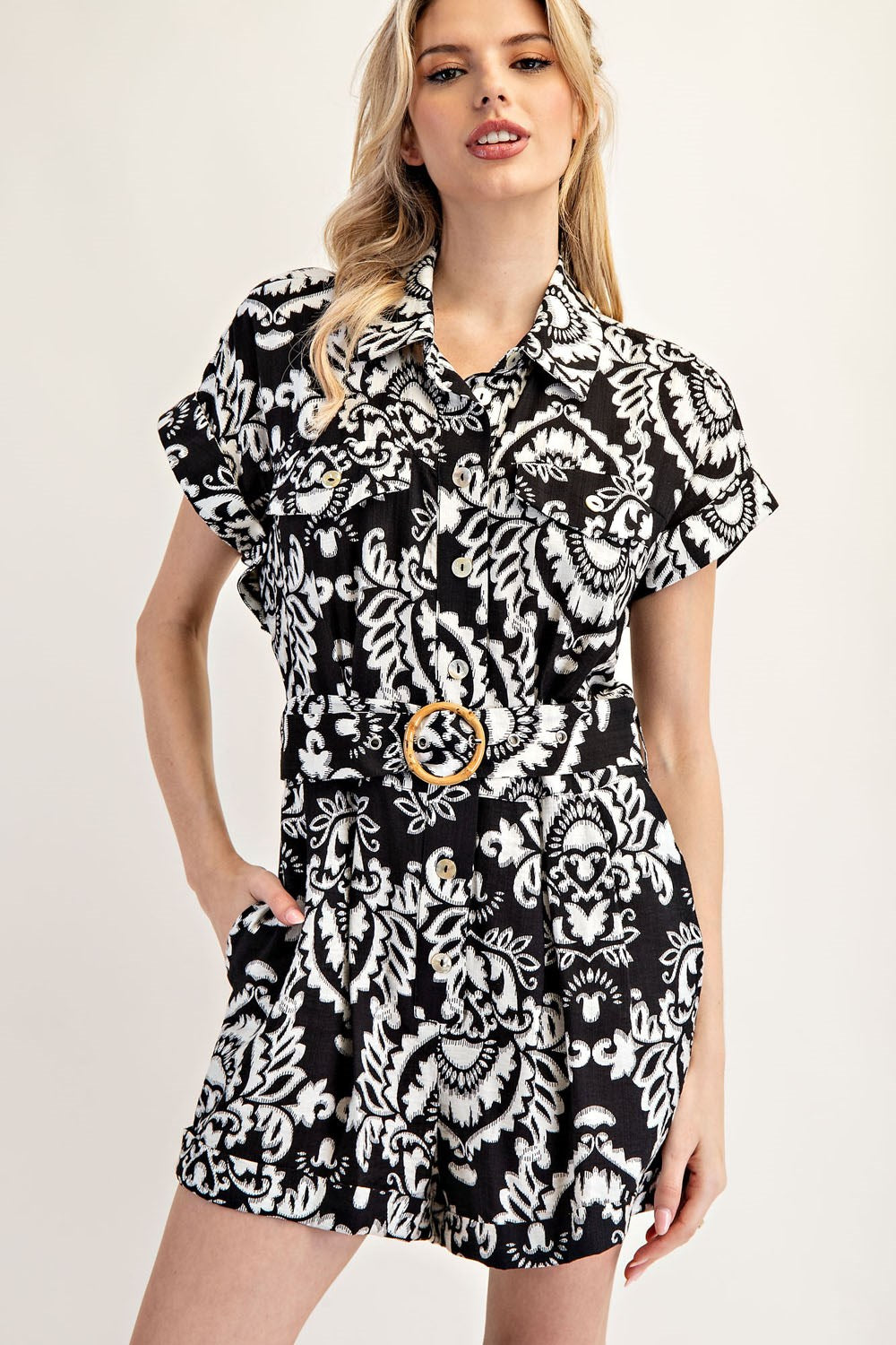 Woman wearing a black and white patterned dress with a belt on a plain background