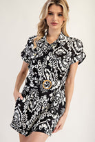 Woman wearing a black and white patterned dress with a belt on a plain background