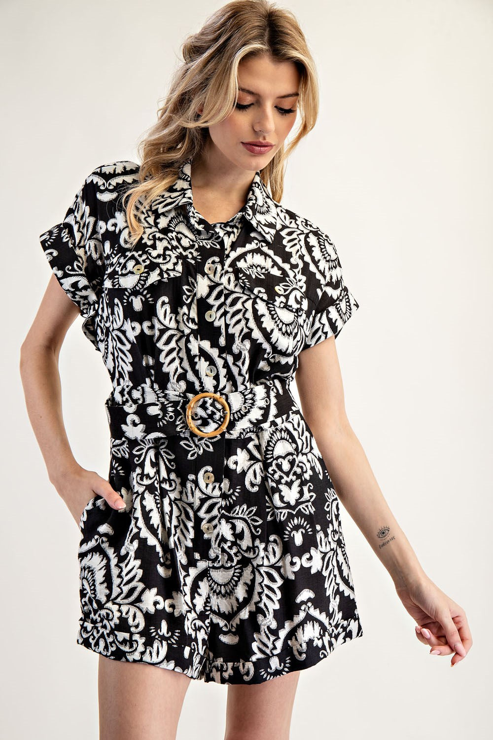 Woman wearing a black and white patterned dress with a belt on a plain background