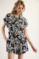 Woman wearing a black and white patterned dress with a belt on a plain background