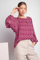 Woman wearing a pink patterned blouse and beige pants against a white background