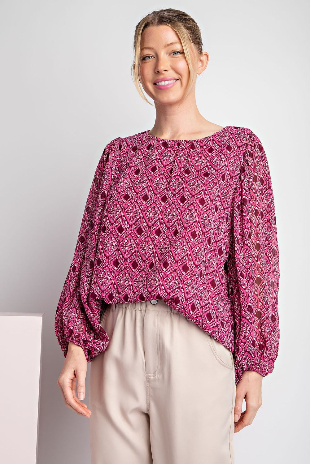 Woman wearing a pink patterned blouse against a plain background