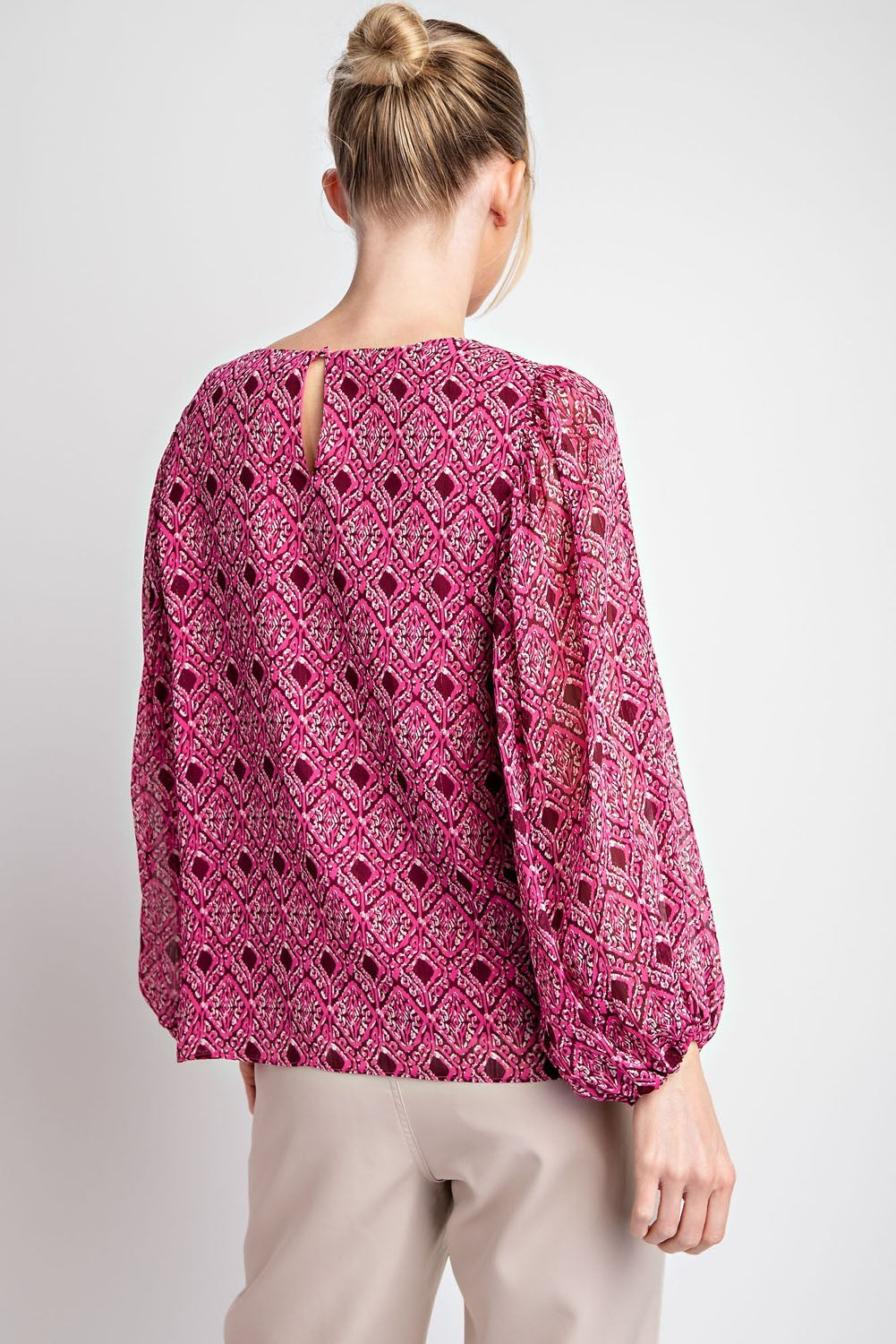 Person wearing a pink patterned blouse on a plain background