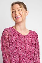 Woman wearing a pink patterned top against a plain background