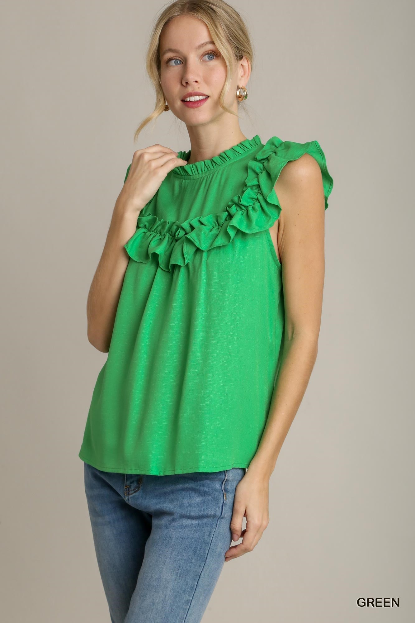 Woman wearing a green top with ruffled details and blue jeans on a beige background