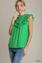 Woman wearing a green top with ruffled details and blue jeans on a beige background