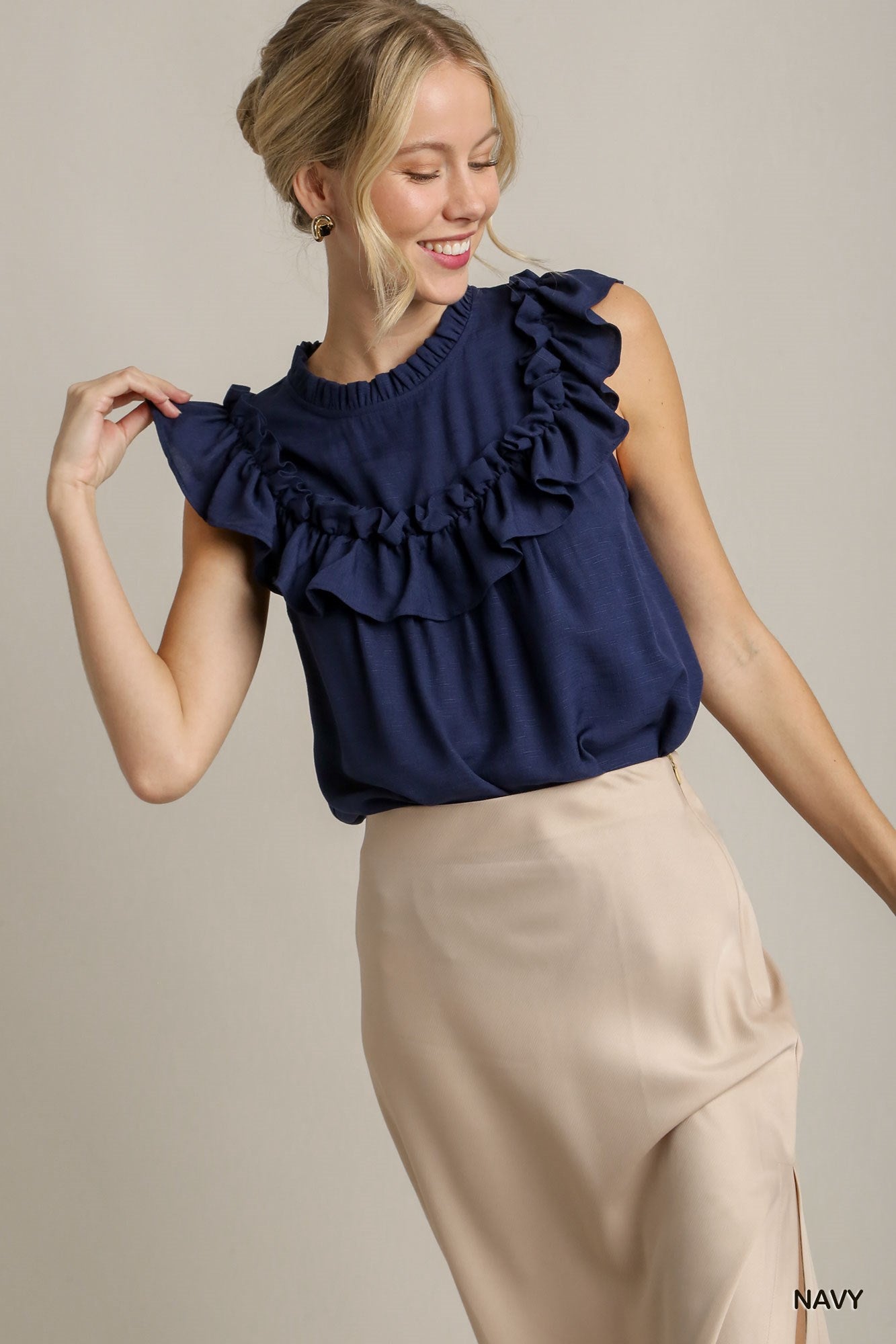 Woman wearing a navy blue ruffled top and beige pants on a plain background