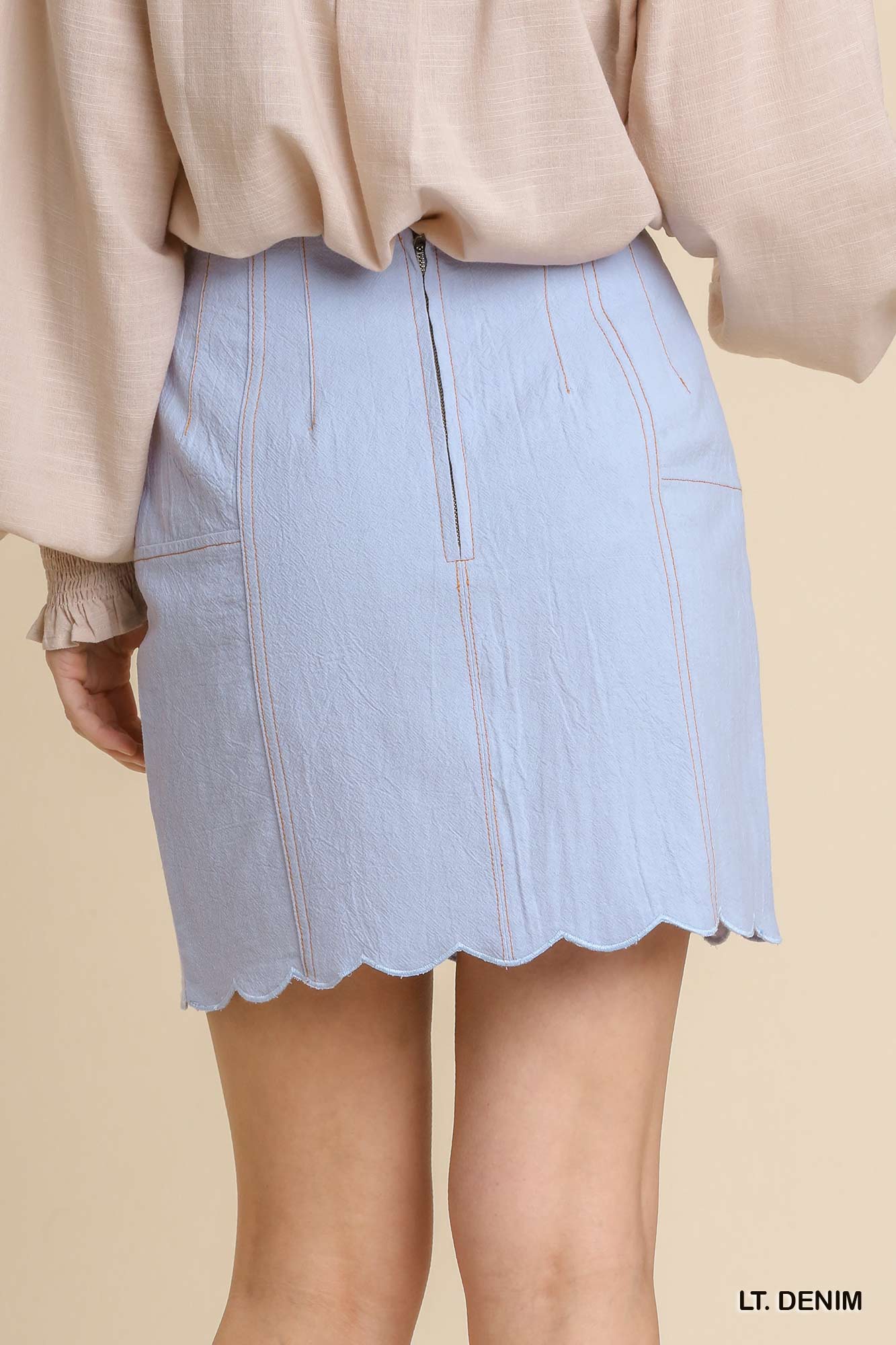 Light denim skirt worn with a beige top on a beige background
