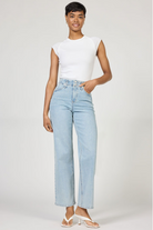 Woman wearing light blue jeans and a white top on a plain background