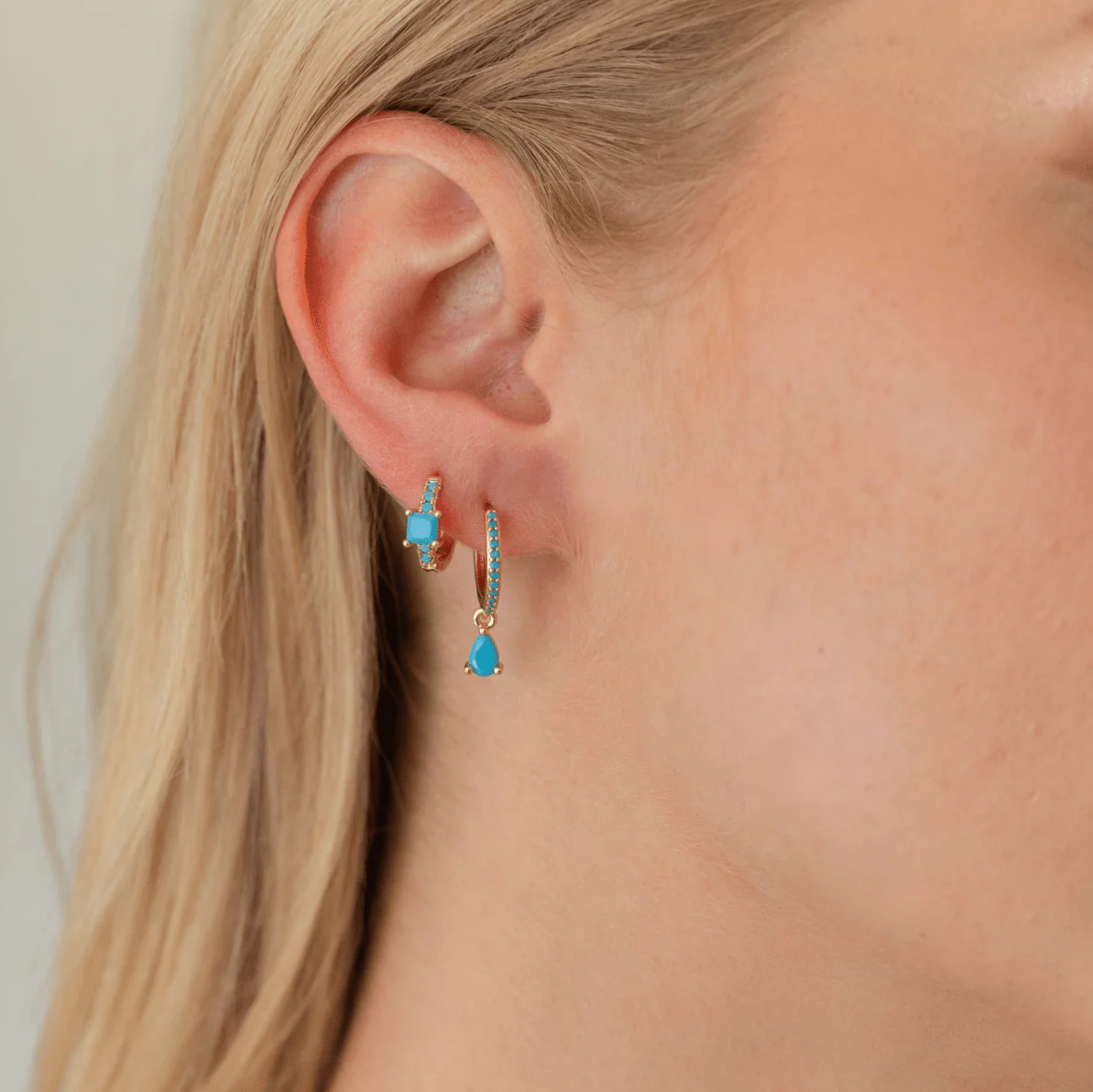 Close-up of a person wearing turquoise earrings with gold accents.