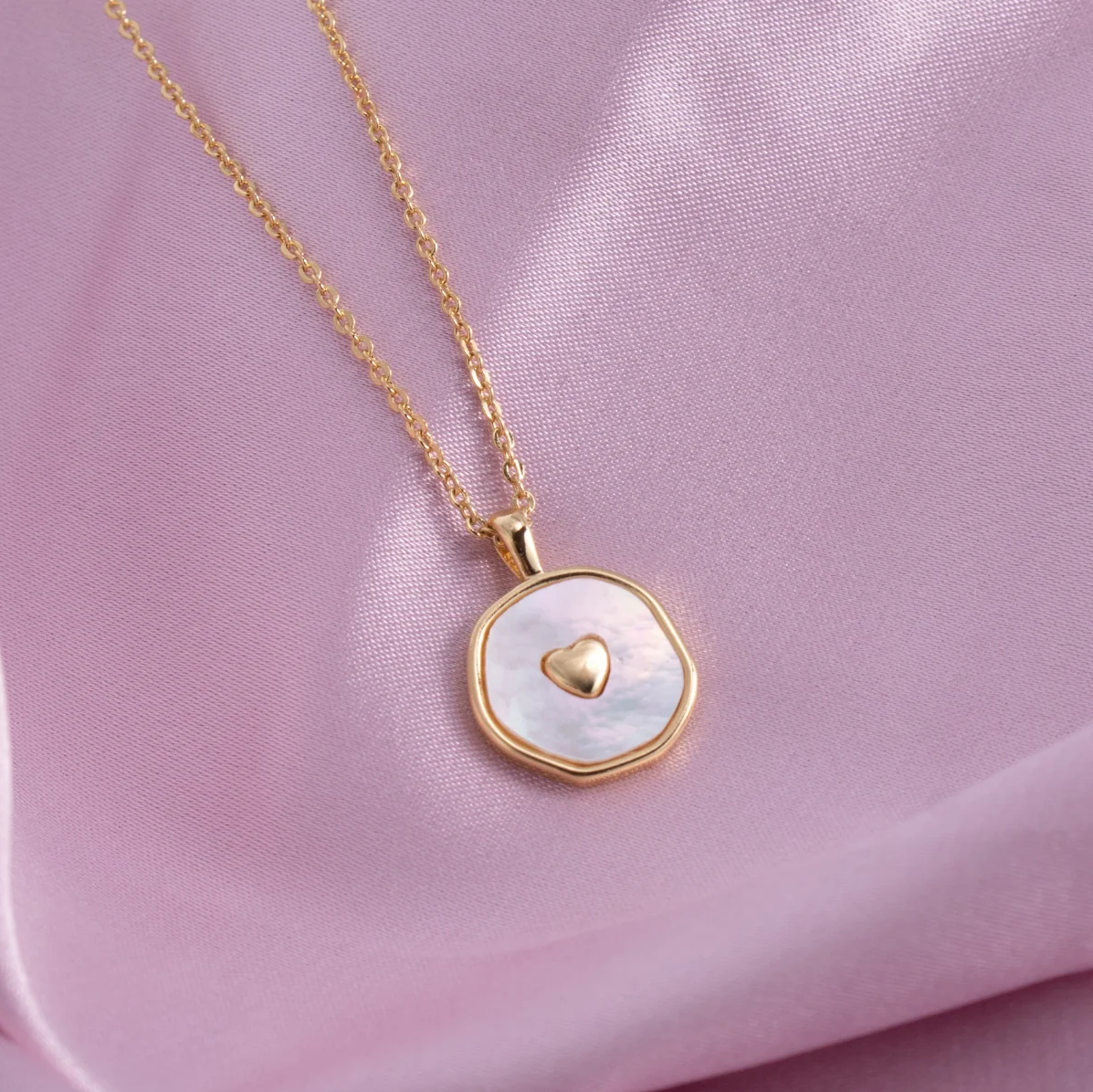 Gold necklace with a heart-shaped pendant on a pink fabric background