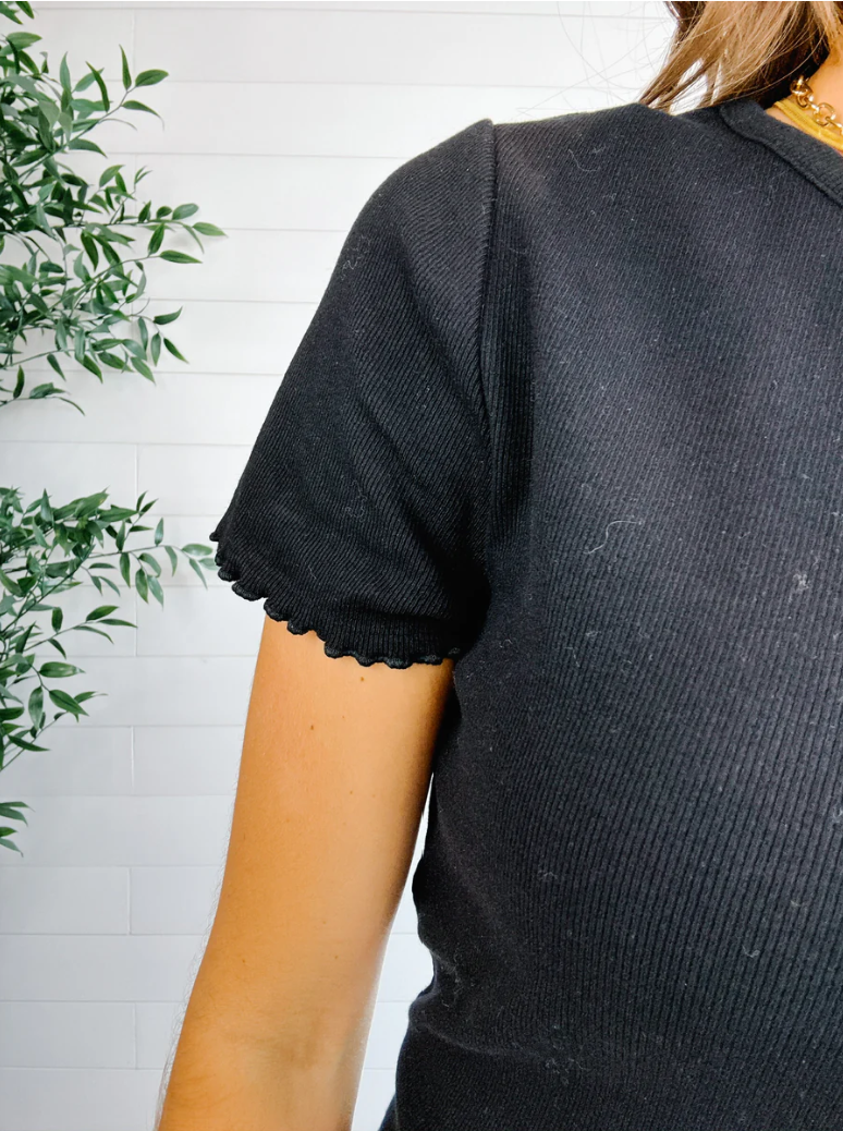 Person wearing a black textured shirt with a white wall and green plant in the background