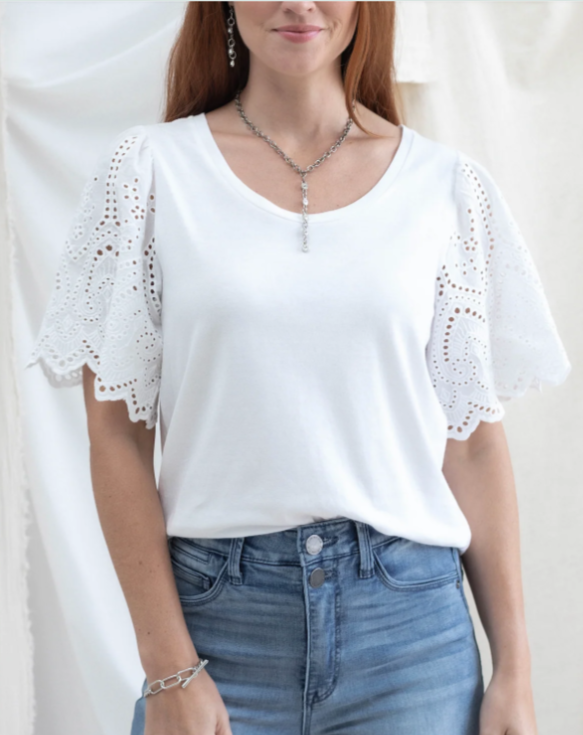 Woman wearing a white blouse with lace details and blue jeans against a plain background