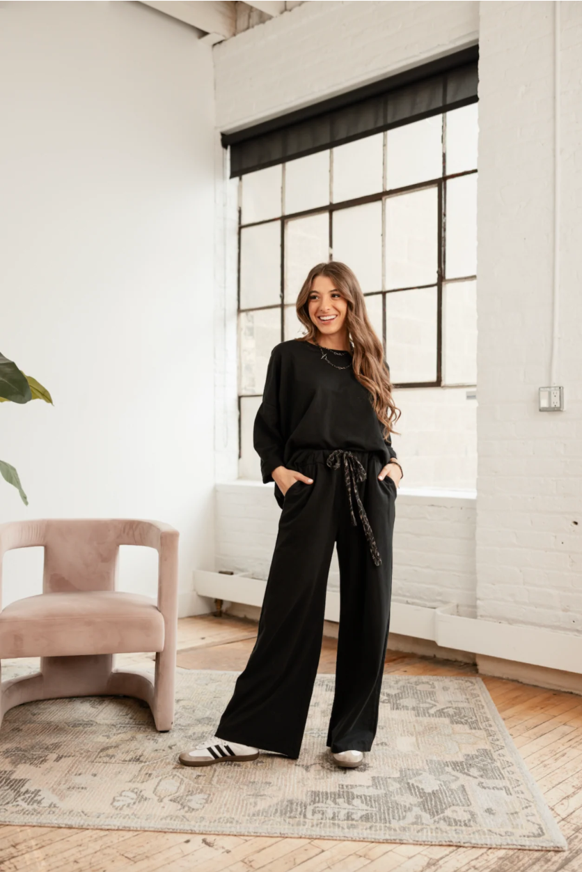 Woman in black outfit standing in a modern room with large windows.