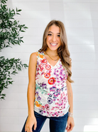 Woman wearing a colorful floral tank top against a white brick wall with a plant to the left.