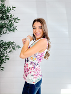 Woman wearing a floral sleeveless top against a white wall with a plant to the left.