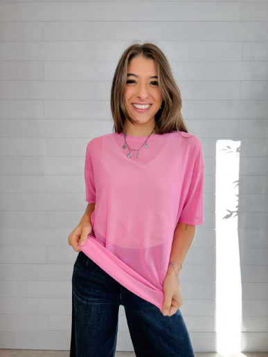 Woman wearing a pink top and blue jeans standing against a gray wall.