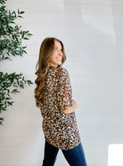 Woman wearing a leopard print shirt standing next to a plant against a white wall