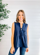 Woman wearing a navy sleeveless top with a white background and green plant.