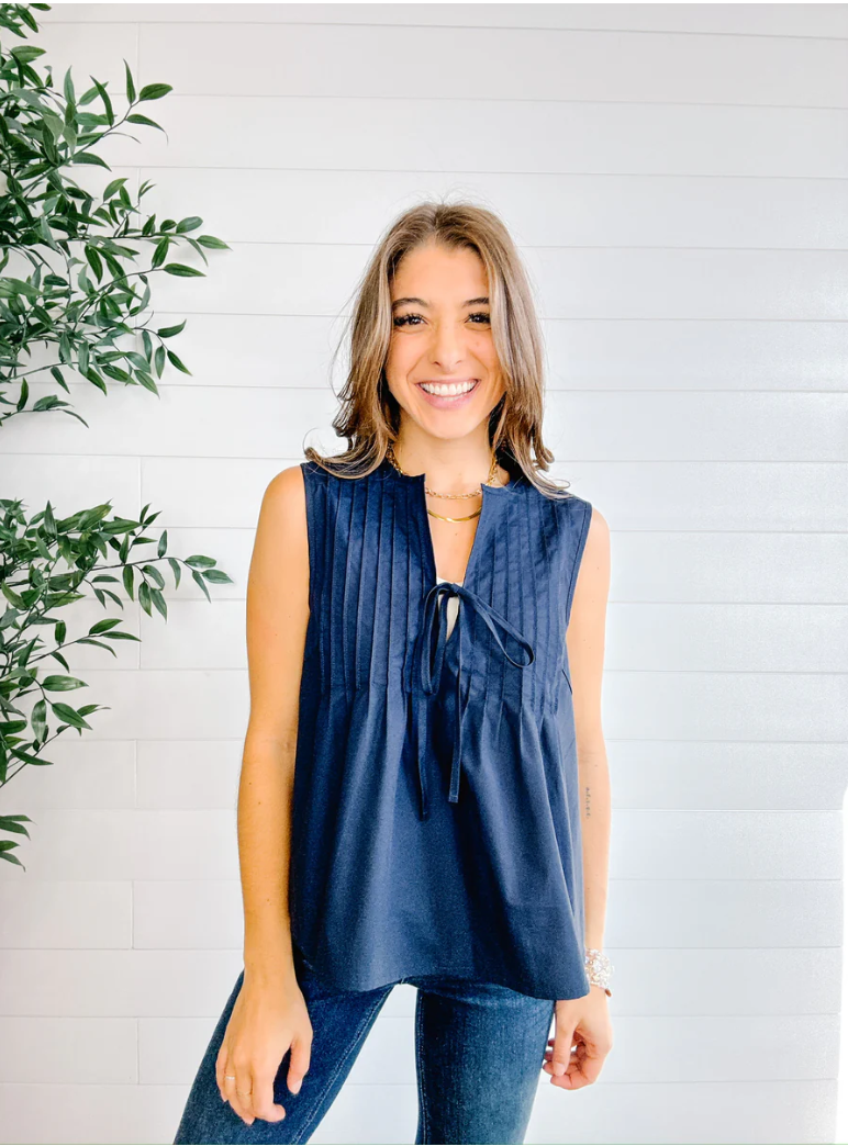 Woman wearing a navy sleeveless top with a white background and green plant.