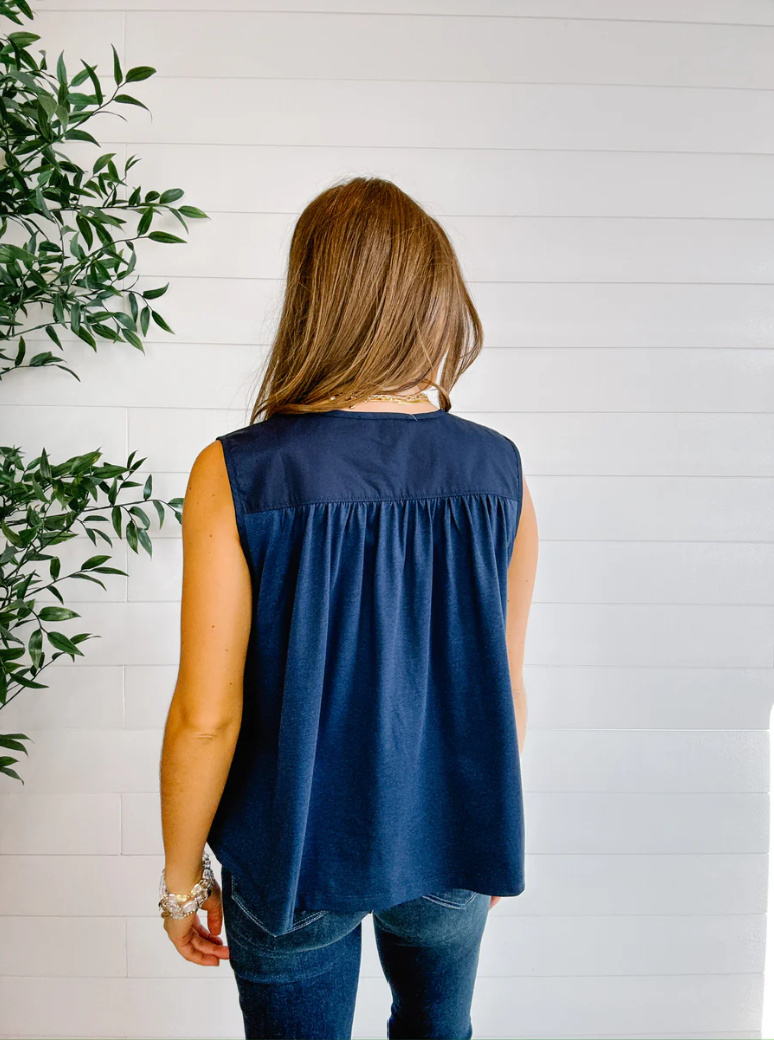 Woman wearing a navy sleeveless top against a white wooden panel background