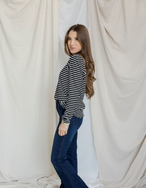 Woman wearing a striped shirt and jeans standing against a white curtain