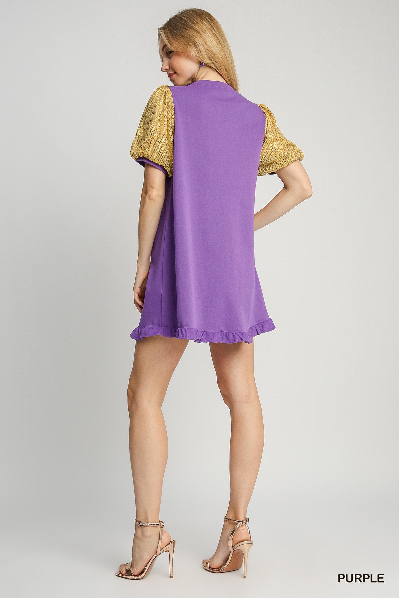 Woman wearing a purple dress with gold sleeves on a gray background