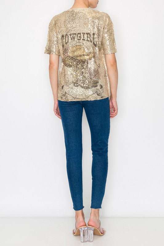 Person wearing a gold sequin 'COWGIRL' top and blue jeans on a white background