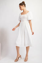 Woman wearing a white dress with puffed sleeves on a plain background