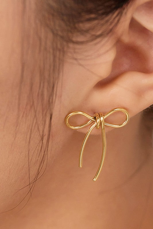 Gold bow-shaped earring worn on an ear with a blurred background