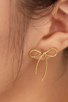 Gold bow-shaped earring worn on an ear with a blurred background