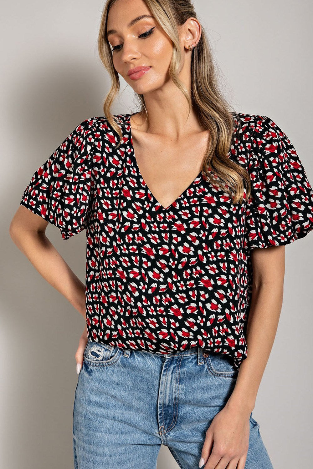 Woman wearing a black patterned top and blue jeans against a neutral background