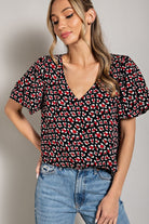 Woman wearing a black patterned top and blue jeans against a neutral background
