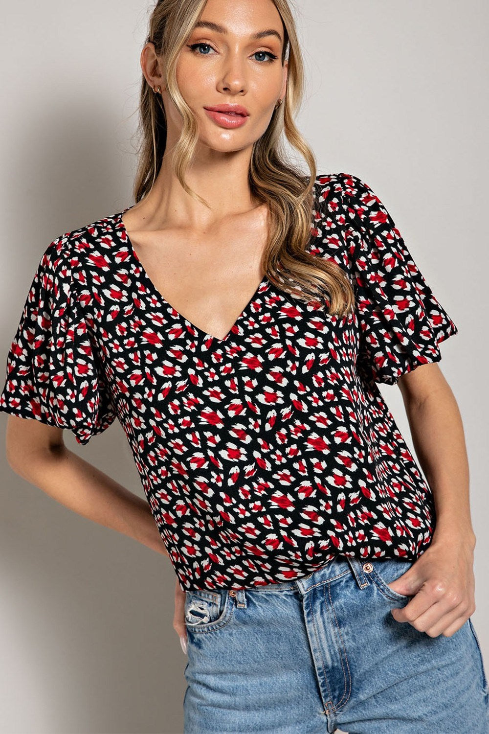 Woman wearing a black patterned top and blue jeans against a plain background
