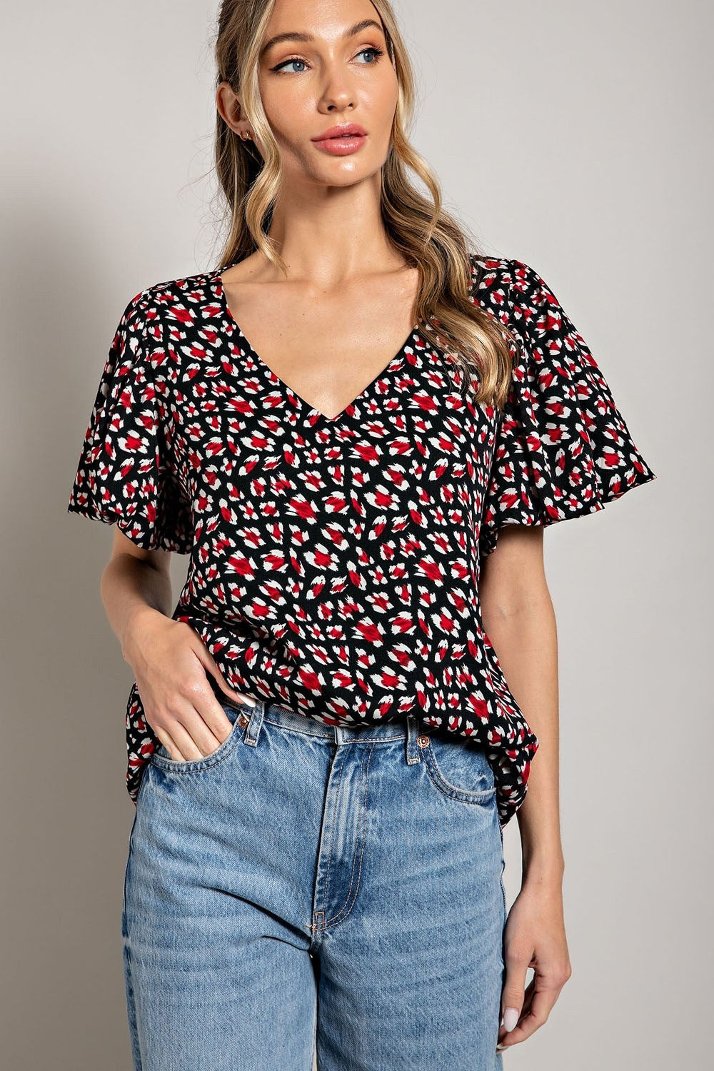 Woman wearing a black floral blouse and blue jeans against a gray background