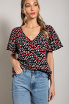 Woman wearing a black floral blouse and blue jeans against a gray background