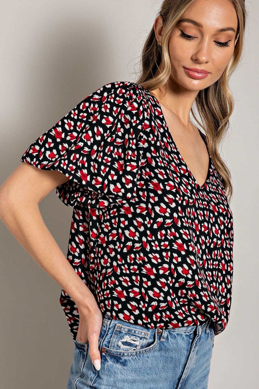 Woman wearing a black patterned top with denim jeans on a neutral background