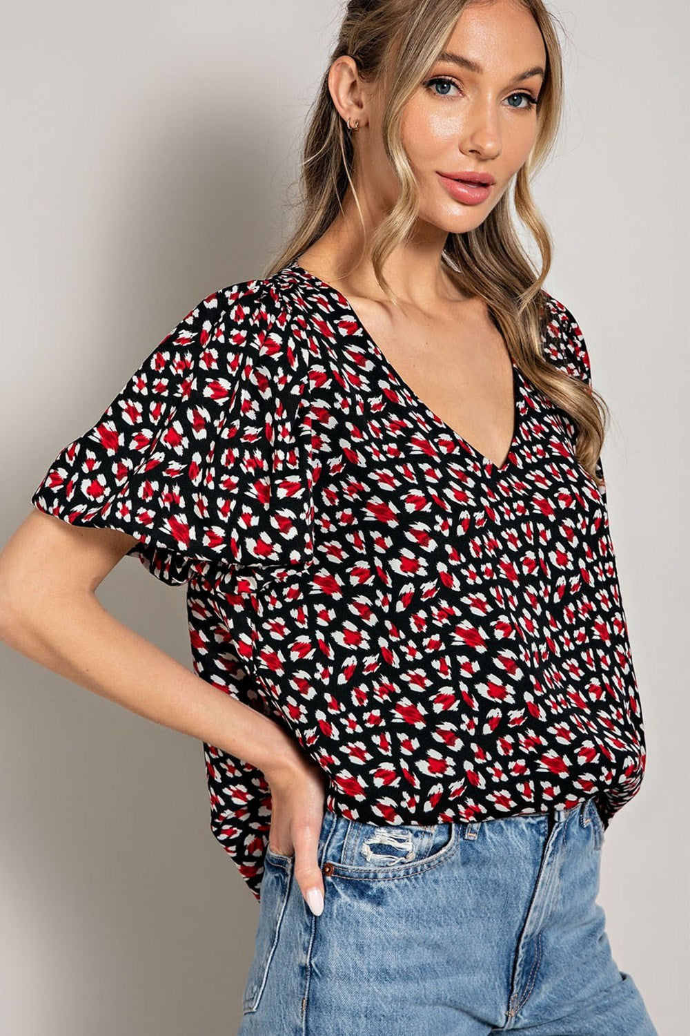 Woman wearing a black patterned top and blue jeans on a plain background