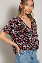 Woman wearing a black patterned top and blue jeans on a plain background